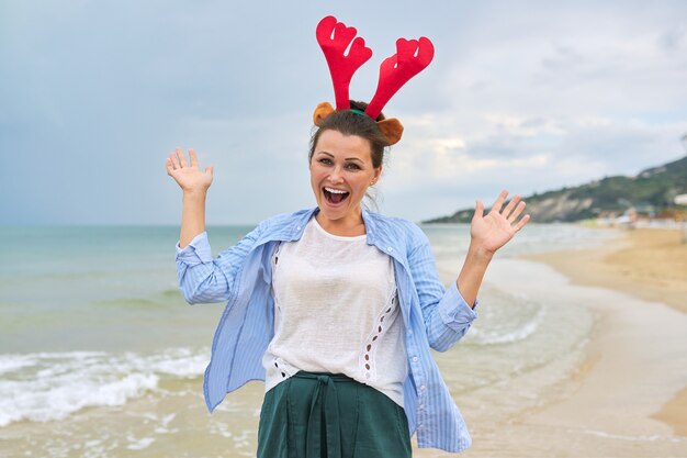 Portrait of happy woman in reindeer ears on the beach smiling