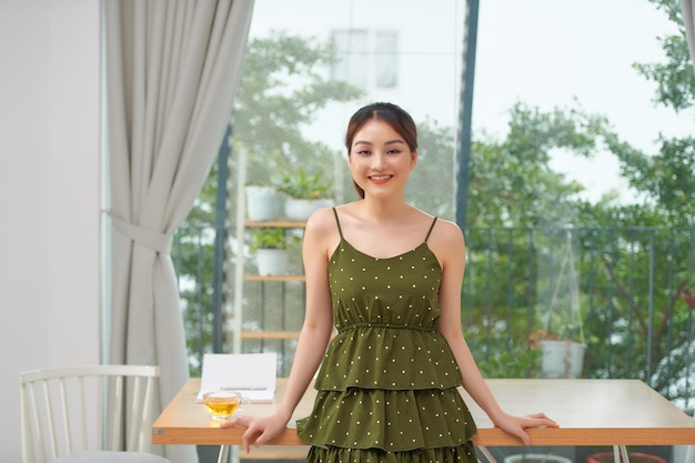 Portrait of a happy woman standing by window smiling with cup of coffee