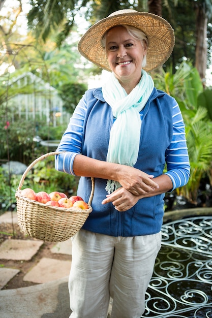 Portrait of happy woman standing with apples at garden