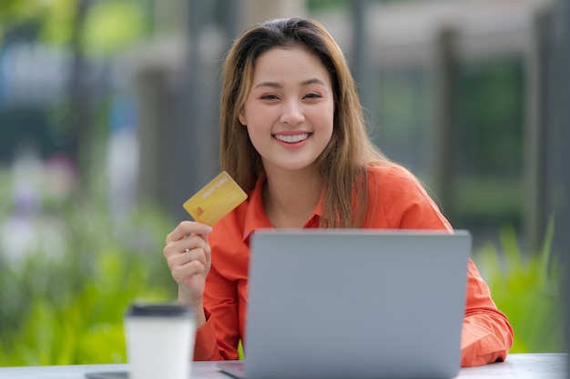 Portrait of Happy woman using laptop with credit card and smiling face at the mall park