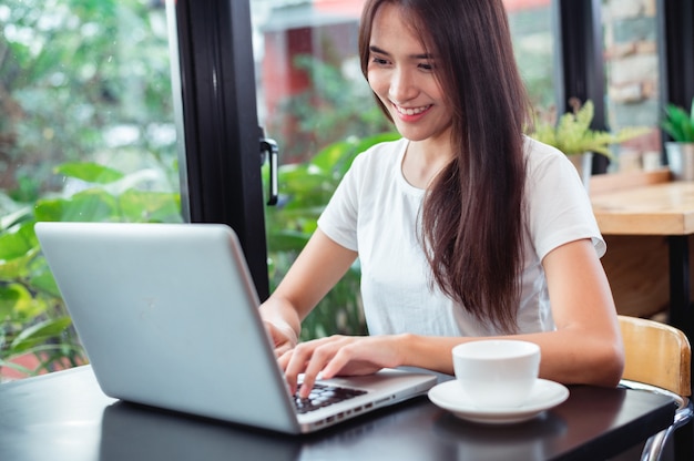 Portrait of a happy woman using a smart phone and a laptop sitting in a table