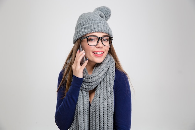 Portrait of a happy woman in winter cloth talking on the phone and  isolated on a white wall