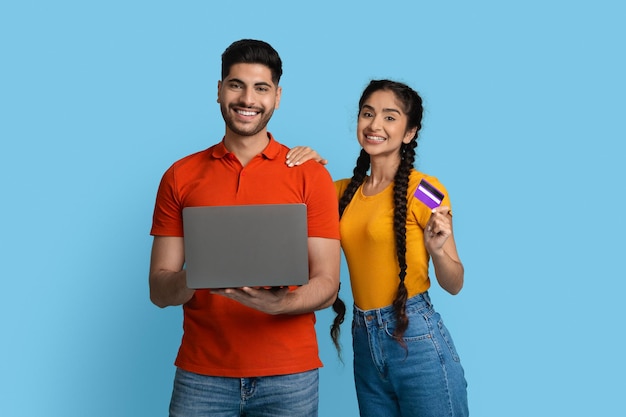 Portrait of happy young arabic couple with laptop and credit card