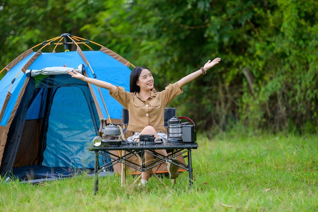 Portrait of happy young asian woman camping alone with open arm sit in front of her tent in campsite