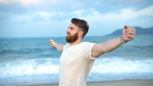 Portrait of happy young bearded guy handsome man on the sea or ocean walking on beach enjoying good summer weather at vacation in tropical country