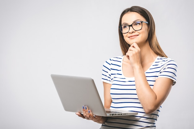 Portrait of happy young beautiful thinking woman standing with laptop