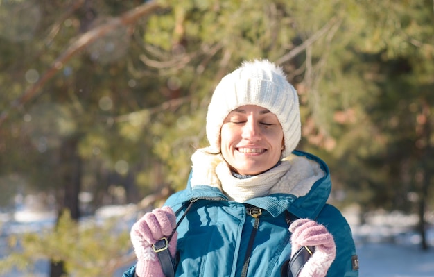 Portrait of a happy young brunette in winter clothes in a white knitted hat in the frost in the sun