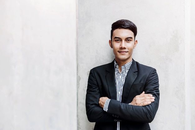 Portrait of Happy Young Businessman standing at the Wall, Smiling and Crossed Arms