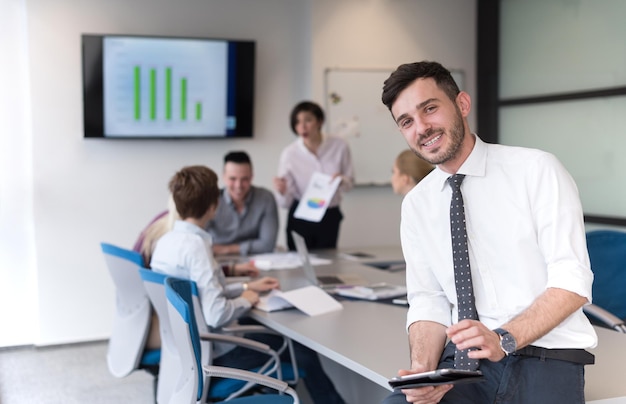 Portrait of happy young businessman with tablet computer office. People group on team meeting in background