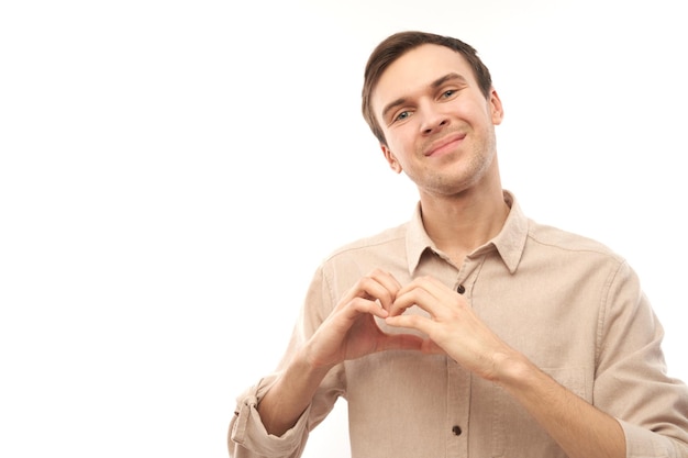 Portrait happy young caucasian man makes heart gesture asks to be my valentine Friend keep hands on chest feel thankful isolated on white studio background