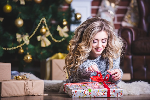 Portrait of a happy young Christmas woman trying to guess what is in the gift box near the Christmas tree