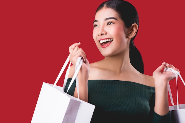 portrait of happy young cute woman posing with shopping bags over Red background.