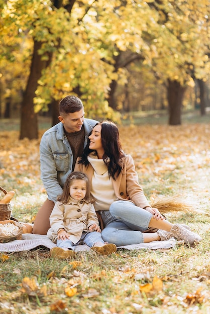 Portrait of happy young family sitting on plaid together in autumn park