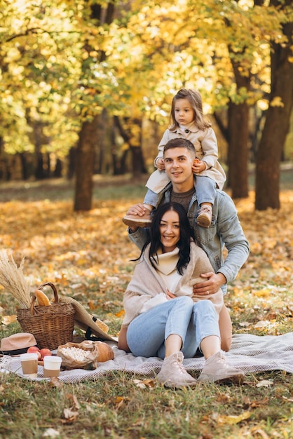 Portrait of happy young family sitting on plaid together in autumn park