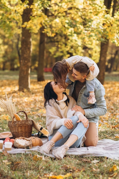 Portrait of happy young family sitting on plaid together in autumn park