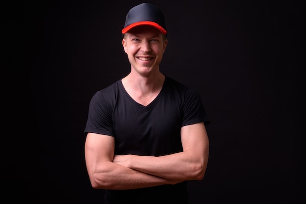 Portrait of happy young handsome man wearing hat and smiling with arms crossed