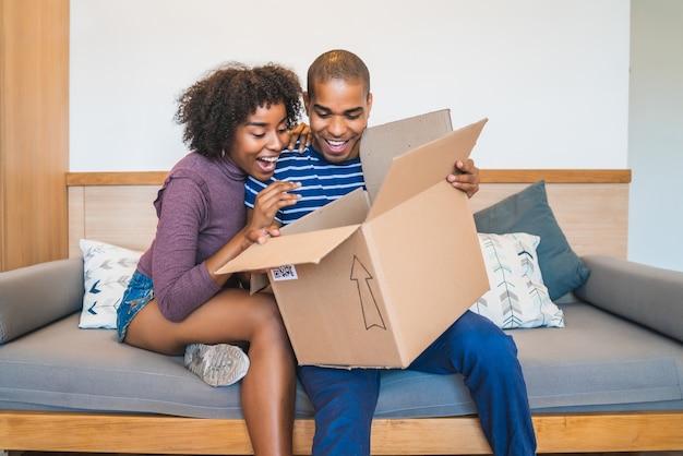 Portrait of happy young latin couple opening a package at home. Delivery, shipping and postal service concept.