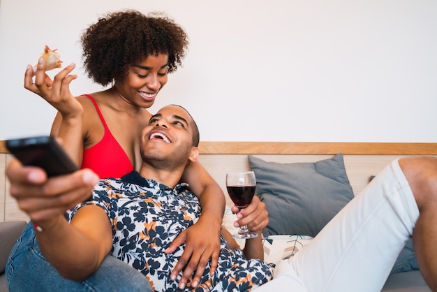 Portrait of happy young latin couple spending time together and watching tv at their home. Lifestyle and relationship concept.