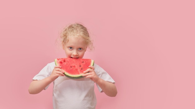 Portrait happy young little girl is holding slice of watermelon over colorful pink background