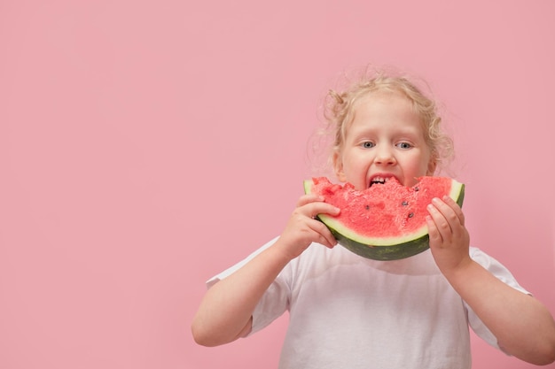 Portrait happy young little girl is holding slice of watermelon over colorful pink background