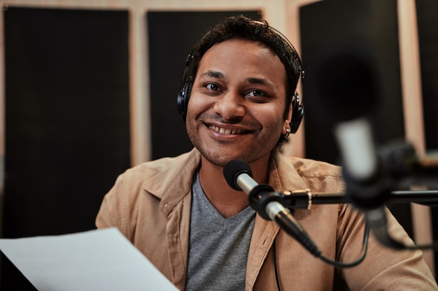 Portrait of happy young male radio host in headphones smiling at camera while talking broadcasting