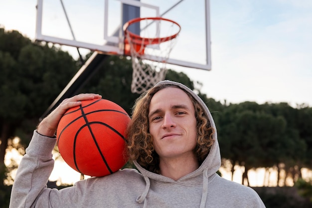 Portrait of a happy young man holding a basketball on a city court concept of urban sport in the street copy space for text