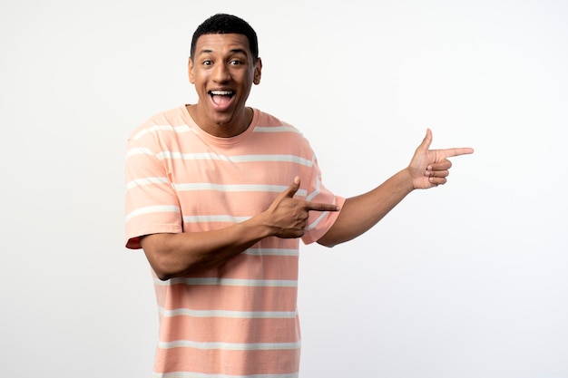 Portrait of a happy young man in pink tshirt pointing fingers away at copy space