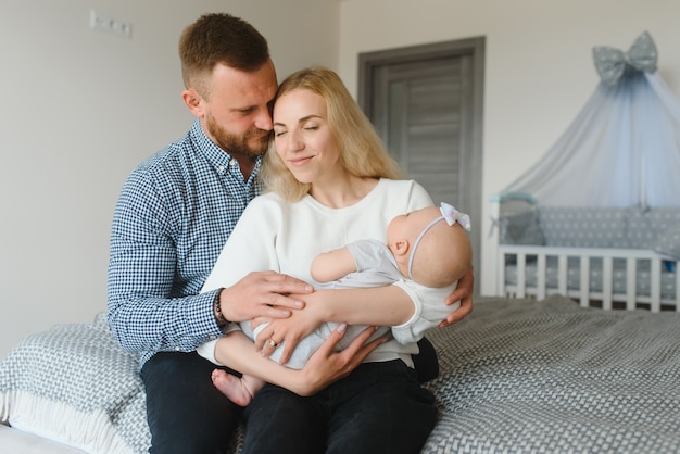 Portrait of happy young parents with baby in the bed at home