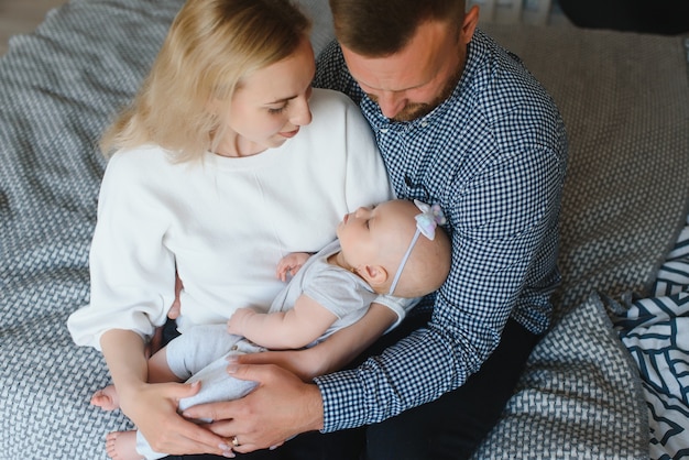 Portrait of happy young parents with baby in the bed at home