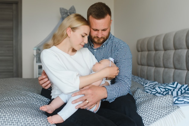 Portrait of happy young parents with baby in the bed at home