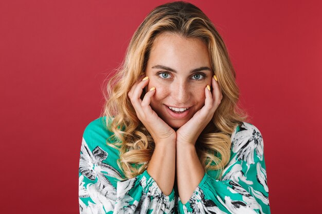 Photo portrait of a happy young pretty blonde cute woman in dress posing isolated over red wall