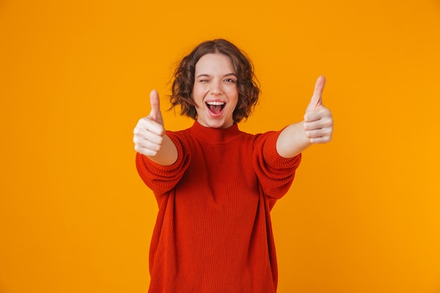 portrait of a happy young pretty woman posing isolated over yellow wall showing thumbs up.