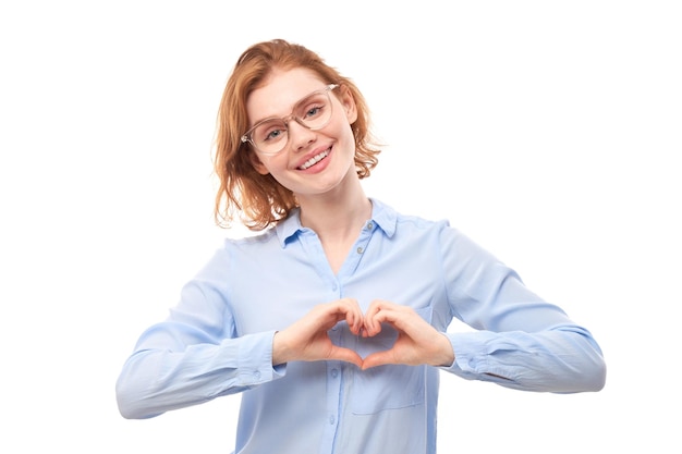 Portrait happy young redhead woman makes heart gesture asks to be my valentine Girlfriend keep hands on chest feel thankful isolated on white studio background