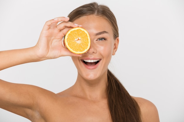 Portrait of a happy young topless woman isolated, holding sliced orange at her face