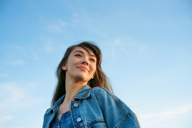 Portrait of a happy young woman in denim jacket against the background of the sky