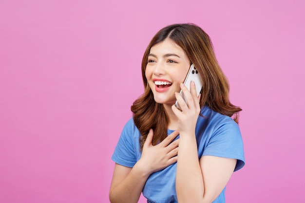 Portrait of happy young woman wearing casual tshirt talking on mobile phone isolated over pink background