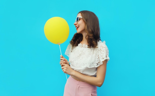 Portrait of happy young woman with yellow balloon on blue studio background