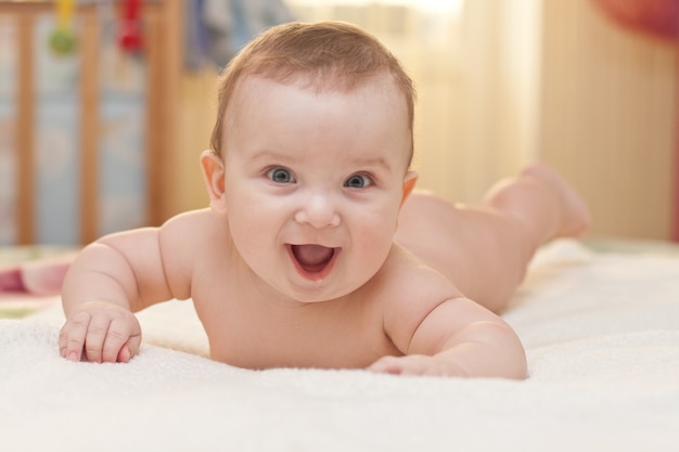 Portrait of healthy and smiling 3-month baby  close up. newborn  boy lying on belly on the bed.