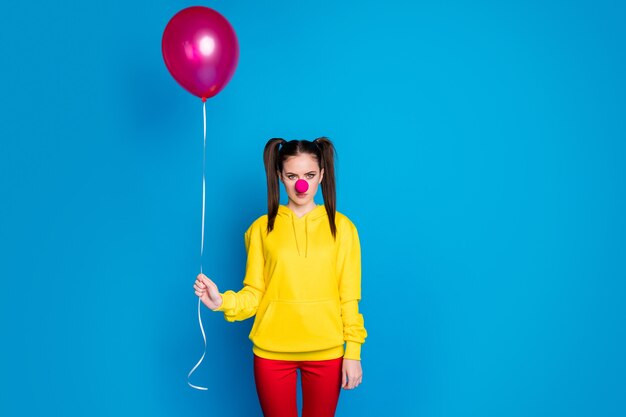 Photo portrait of her she nice attractive sad bored sullen gloomy girl circus clown holding in hand helium ball dull event occasion isolated over bright vivid shine vibrant blue color background