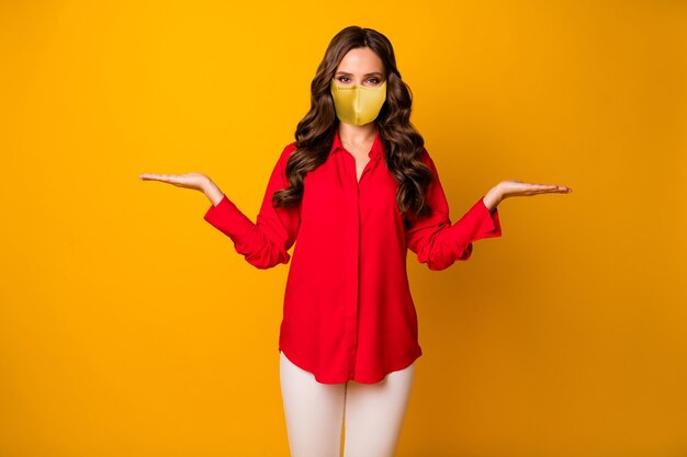 Photo portrait of her she nice-looking attractive wavy-haired girl wearing safety reusable textile mask holding on palms copy space mers cov isolated bright vivid shine vibrant yellow color background