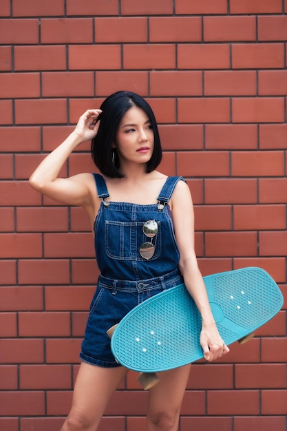 Portrait of hipster girl with skateboard on brick wall backgroundBeautiful asian woman pose for take a photo