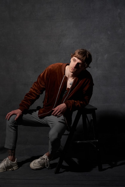 Portrait of a hipster person with tattooed body in jacket poses in dark background