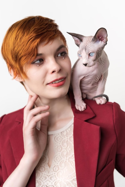 Portrait of hipster redhead young woman with short hair dressed in red jacket and playful sphynx cat