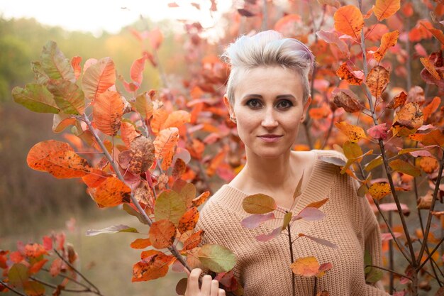 Portrait of hipster woman with short hair in autumn park background with red and golden trees