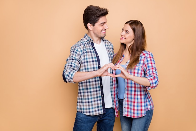 Portrait of his he her she nice attractive lovely tender sweet gentle cheerful couple wearing checked shirt showing heart figure honey moon isolated over beige pastel color background