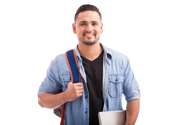 Portrait of Hispanic guy going to a university carrying a backpack and a laptop computer on a white background