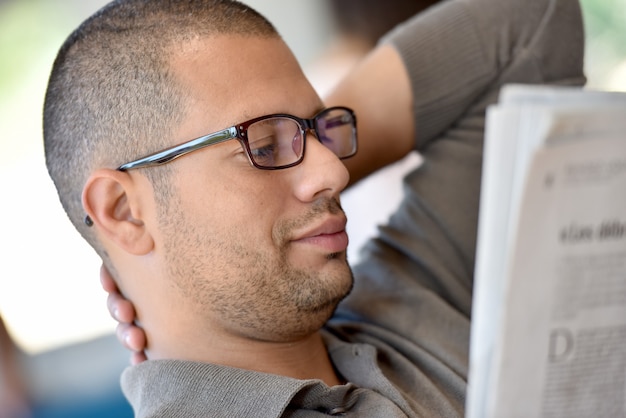 Portrait of hispanic guy with eyeglasses reading newspaper