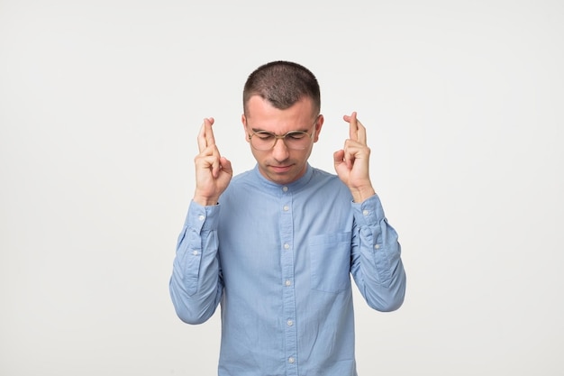 Portrait of hispanic young man in blue shirt holding fingers crossed for good luck