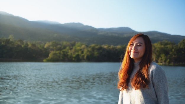 Portrait image of a beautiful asian woman standing in front of the lake and mountains before sunset