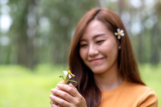 Portrait image of a beautiful young asian woman holding Biden Alba or Spanish needles flower in the park